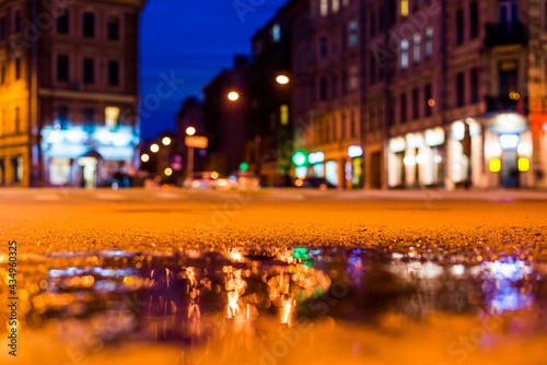 Nights lights of the big city, the empty night crossroad between buildings. Close up view of a puddle level