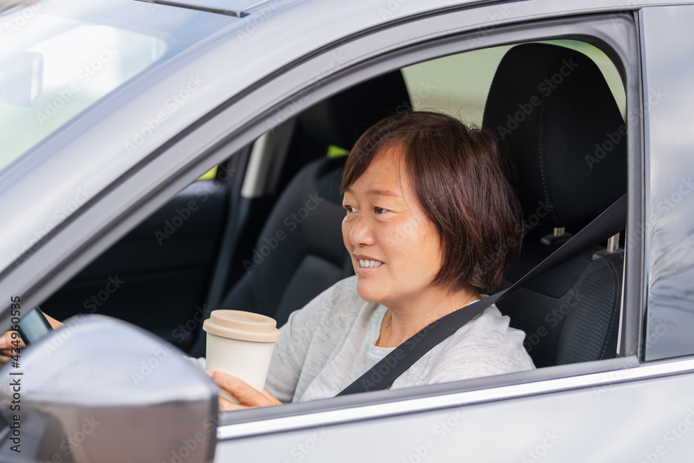 A mature asian woman in a car holding a paper cup: Selective focus. Lifestyle concept.