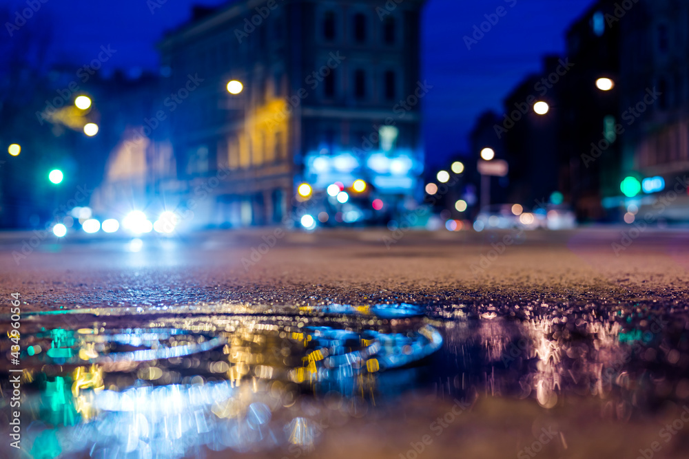Nights lights of the big city, the night intersection between the houses on which cars travel. Close up view  of a puddle on the level of the hatch