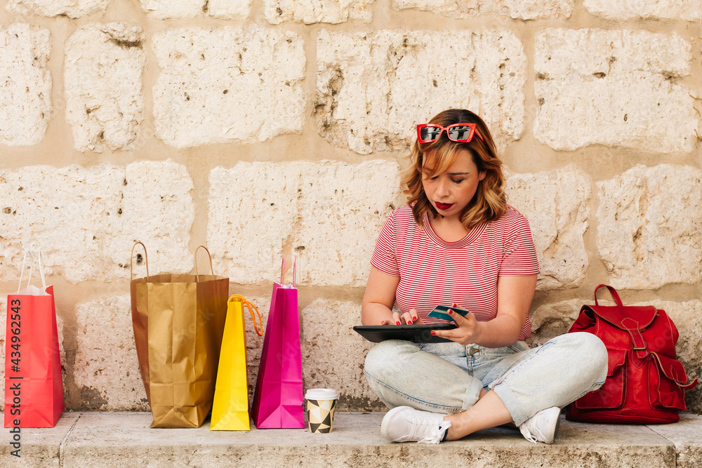 Woman buying online from her mobile device or tablet with her credit card in the street. lifestyle concept. colored bags and shopping Woman buying online from her mobile device or tablet with her credit card in the street. lifestyle concept. colored bags and shopping
