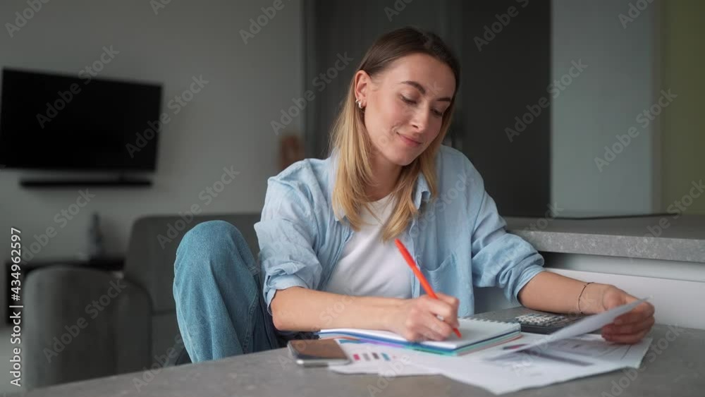 A pensive woman writing bills in a notebook while sitting at the table in the room A pensive woman writing bills in a notebook while sitting at the table in the room
