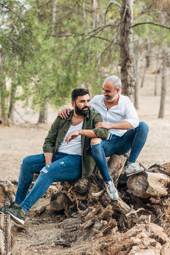 Gay lgbt male couple sitting outside. lgbtq friends hugging in the park. Stylish men with beards. 