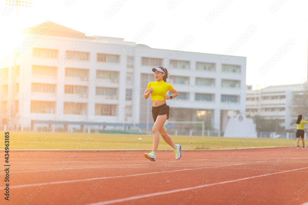Young Asian woman in yellow sportswear runs on the track in the stadium in the morning.