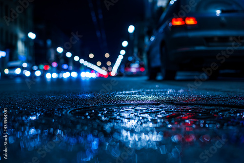 Nights lights of the big city, the city street with parking car. Close up view of a puddle on the level of the hatch