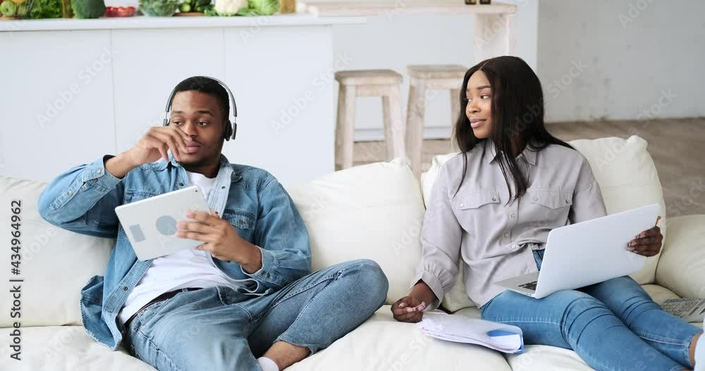 Woman working on laptop having fun with husband in headphones using digital tablet at home Woman working on laptop having fun with husband in headphones using digital tablet at home