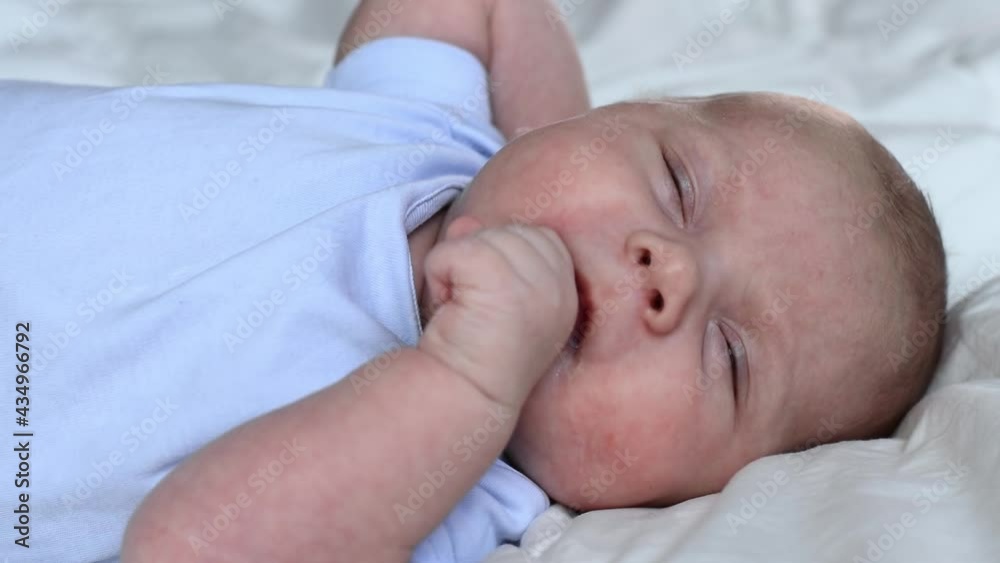 Newborn baby portrait. Close up face infant baby laying on a soft blanket. One month child waking up, opening eyes, yawning and smiling. Hungry little child sucking fingers. Infancy concept. Newborn baby portrait. Close up face infant baby laying on a soft blanket. One month child waking up, opening eyes, yawning and smiling. Hungry little child sucking fingers. Infancy concept.