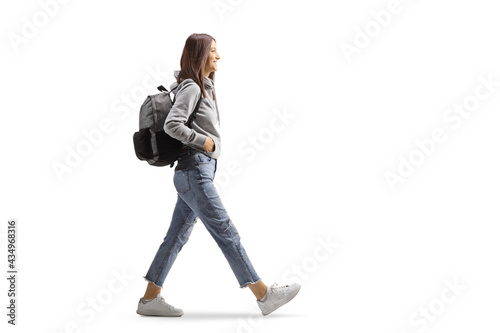 Full length profile shot of a female student in jeans and gray hoodie walking with a backpack