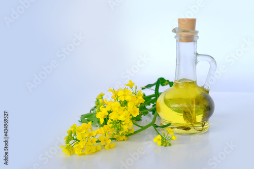 close-up of appetizing yellow oil in a bottle, glass jug, bright rapeseed flowers, vegetable oil cooking concept, cooking healthy food at home, selling nature products photo