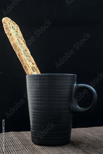 Foto Taza o jarra de desayuno con media baguette tostada emergiendo de su boca, todo ello descansando sobre un esterilla individual