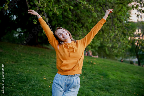 A young European happy woman wearing orange hoodie looking straight. A fun picture with a model on a bright summer day with her hands up. Colourful fun photo. Copy space for text.