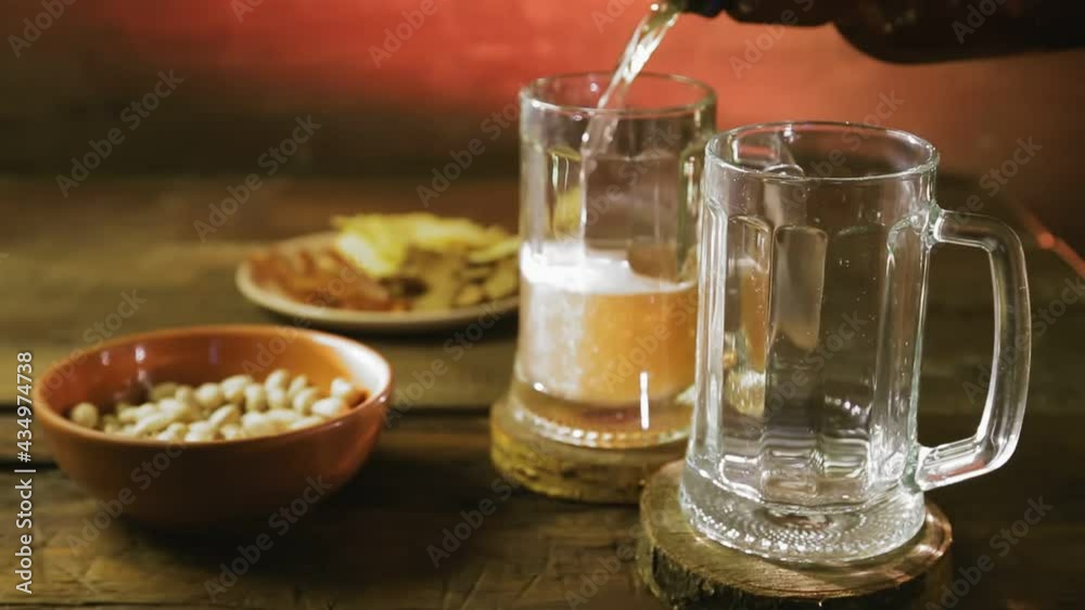 Foaming cold light beer is poured into mugs on a wooden table. Foaming cold light beer is poured into mugs on a wooden table.