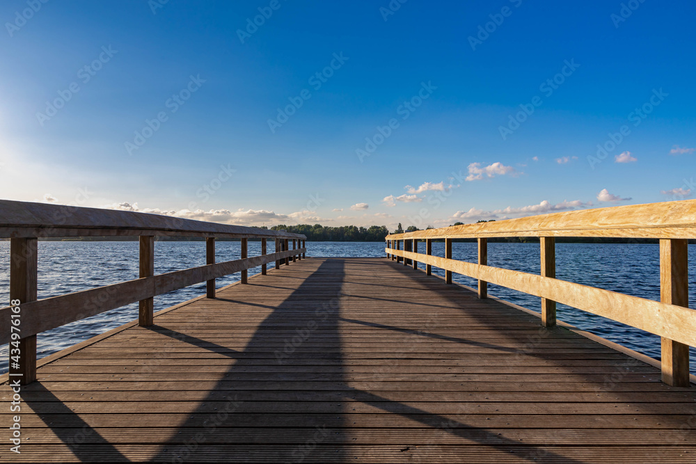 Summer landscape with wooden jetty (pier) extend into the Nieuwe meer (New lake) is in southwest of Amsterdam, Beautiful blue sky with golden sunlight before the sunset, Amsterdamse Bos.