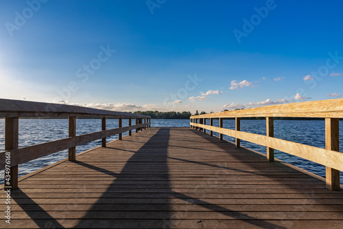 Summer landscape with wooden jetty (pier) extend into the Nieuwe meer (New lake) is in southwest of Amsterdam, Beautiful blue sky with golden sunlight before the sunset, Amsterdamse Bos. © Sarawut