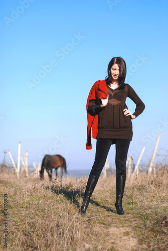 woman with red coat standing in field with horse