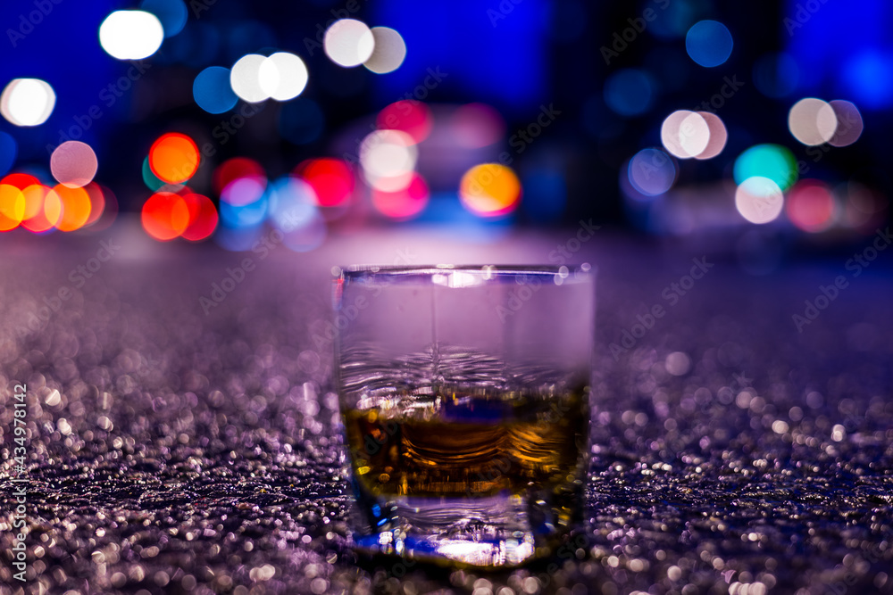 Lights of the city at night through the glass of alcohol, parking lights of the cars. View from the glass level with brandy standing on the asphalt Lights of the city at night through the glass of alcohol, parking lights of the cars. View from the glass level with brandy standing on the asphalt