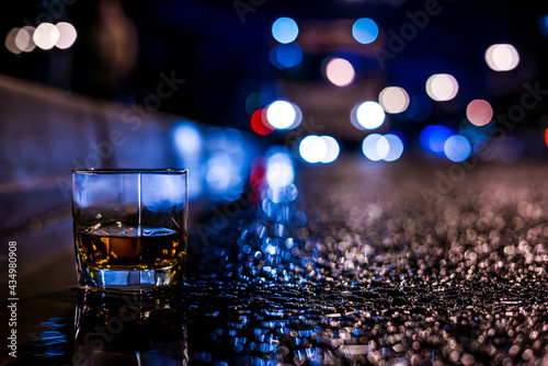 Lights of the city at night through the glass of alcohol, headlights of the approaching bus. Close up view of a glass of brandy level standing near the curb