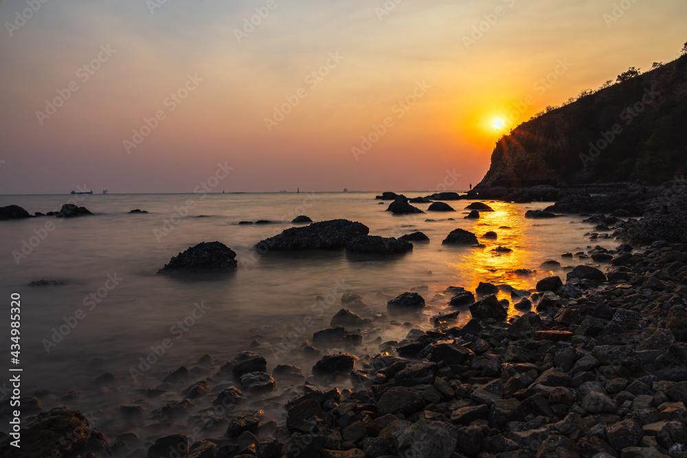 Coast in the summer of Thailand At sunset that is shining through the mountains and beam of light hitting the sea and rocks to create a beautiful ray, Sunset also turns the sky into a beautiful colo
