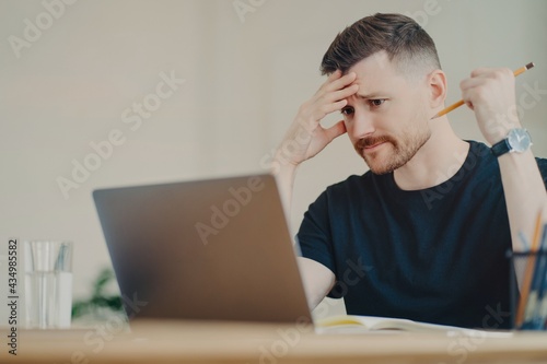 Stressed male office worker looking at laptop with worried face expression photo
