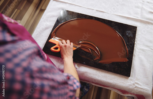 Top view of chocolatier holding cake scraber and cooling melted chocolate mass on a marble table photo