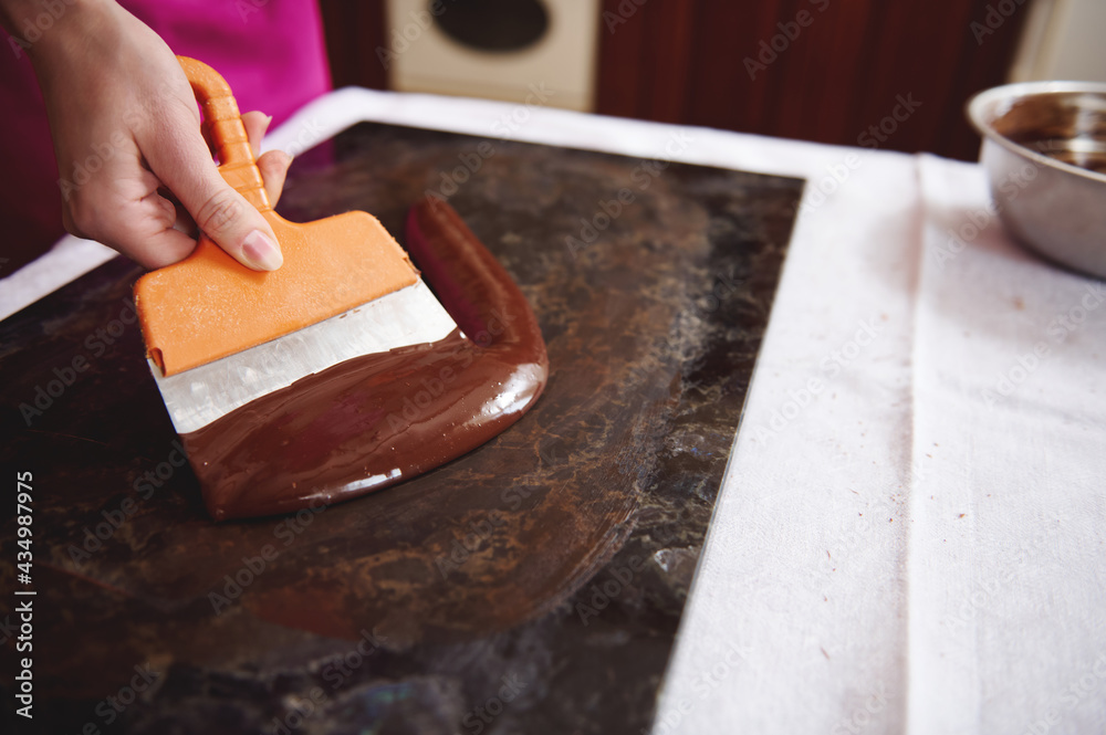 Confectioner working on tempering melted chocolate mass on a marble table Confectioner working on tempering melted chocolate mass on a marble table