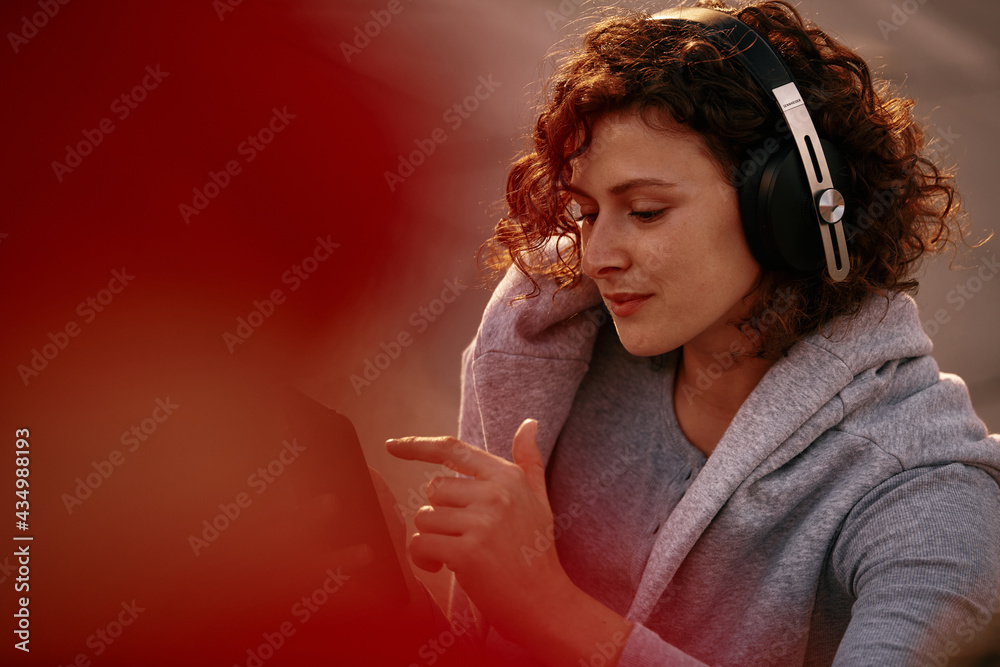 Portrait of a young woman with curly hair, dressed casually sitting on the street and listening to music. She is holding the phone in her hands. Portrait of a young woman with curly hair, dressed casually sitting on the street and listening to music. She is holding the phone in her hands.