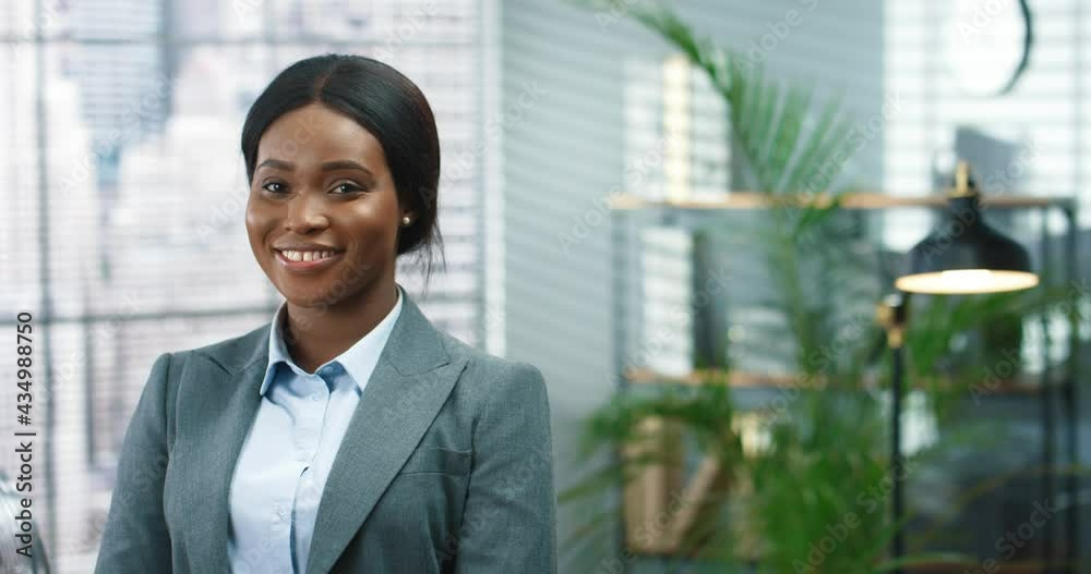 Close up portrait of young beautiful happy female worker looking at camera and smiling in cabinet. African American woman entrepreneur in room at workplace, businesswoman, professional concept Close up portrait of young beautiful happy female worker looking at camera and smiling in cabinet. African American woman entrepreneur in room at workplace, businesswoman, professional concept