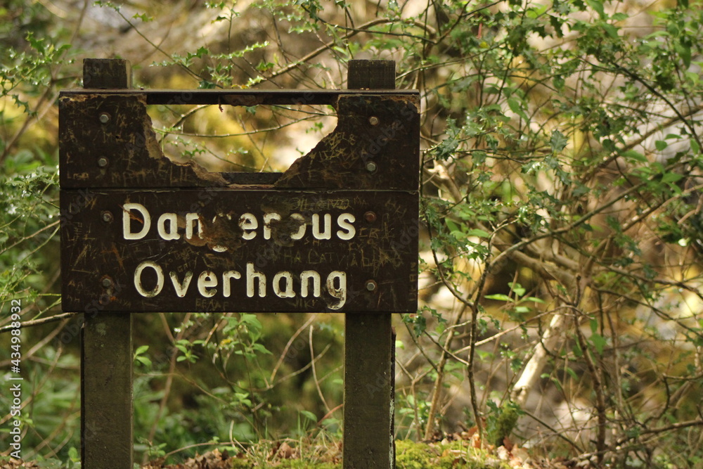 dangerous overhang sign close up with trees in background
