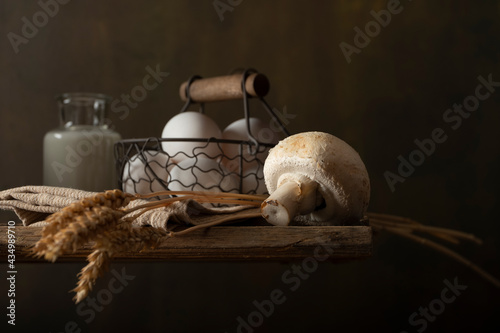 Still life composition with farm products on wooden table. Basket with eggs, bottle with milk, mushroom, wheat ears.