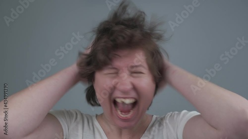 Crazy young toothless female screaming and laughs, pulling hair. Emotionally unstable, insane female with disheveled hair and half front tooth instudio on gray background. Grimace. facial expressions photo