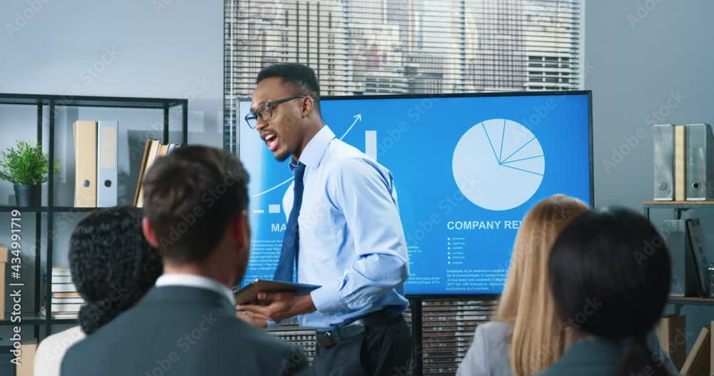 African American young handsome successful male business trainer speaking with employees making presentation to colleagues in office. Businessman presenting new development strategy project