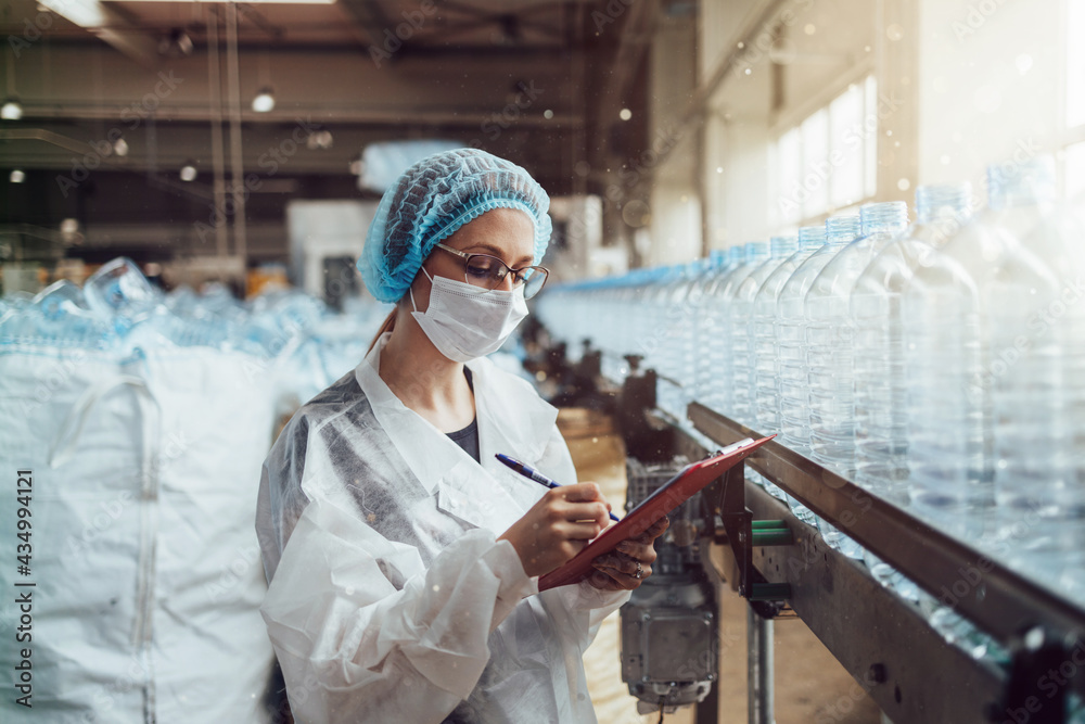 Female worker with protective face mask working in medical supplies research and production factory and checking canisters of distilled water before shipment. Inspection quality control. Female worker with protective face mask working in medical supplies research and production factory and checking canisters of distilled water before shipment. Inspection quality control.