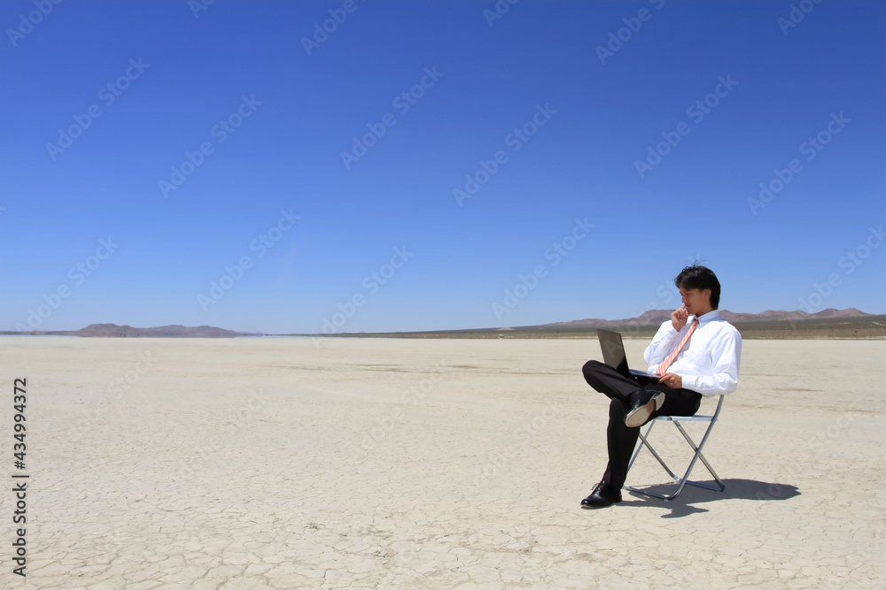 A young Japanese businessman is working on a personal computer in a huge desert A young Japanese businessman is working on a personal computer in a huge desert