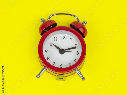 Red alarm clock on yellow background with copy space