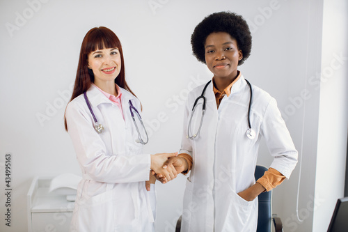 Multiethnic team of doctors. Healthcare and professionalism concept. Cooperation and teamworking. Two diverse confident women doctors  afro american and european  handshaking in the hospital room
