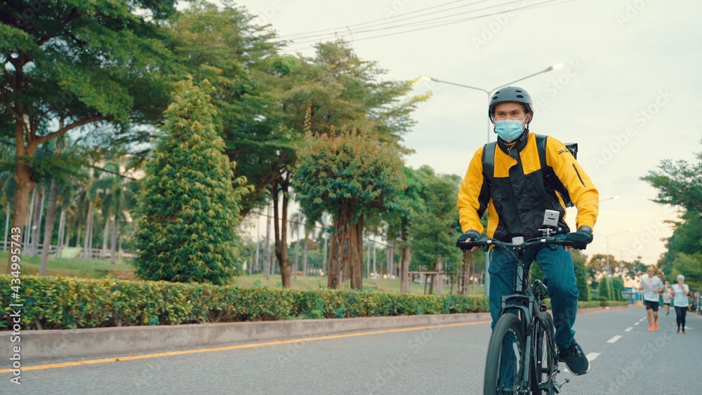 Fototapeta premium Bike delivery person on the move through the city. Young Asian man working as a food delivery person. He riding a bike for sustainable way, Quarantine, Social Distancing.