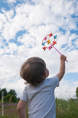 Small kid holding colorful bright rainbow toy pinwheel against blue sky with clouds