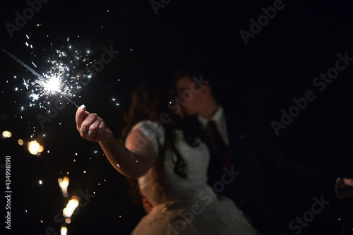 lovers hold burning sparklers in their hands. sparks from a sparkler candle illuminate the bride and groom who are kissing. evening completion of the wedding