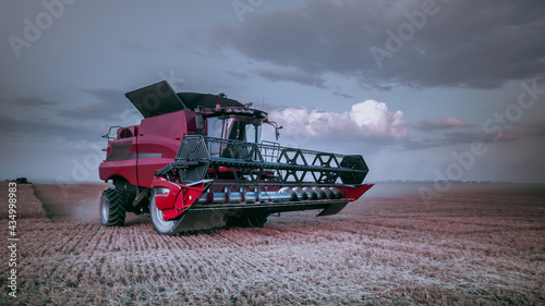 Evening mechanized harvesting of grain in an agricultural field. Bright, summer landscape with a red harvester. Beautiful rural background, wallpaper, design. Selective, soft focus. Photo tinting.