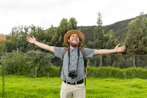 young traveler with glasses and hat smiling with open arms enjoying the air and nature