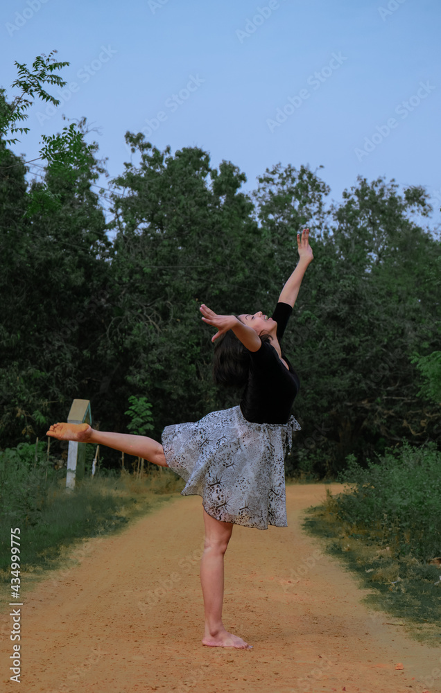 Naklejka premium Full-length portrait of a beautiful young girl ballerina gracefully dancing in nature | teen girl creatively in motion doing a gymnastic pose at outdoor