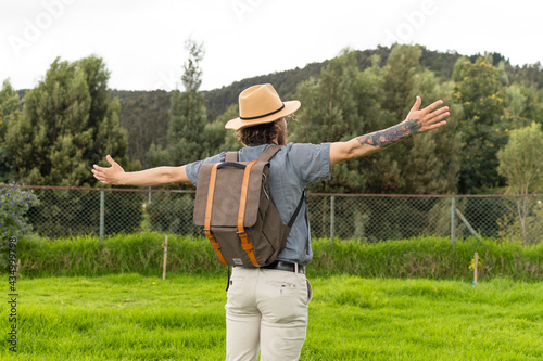 traveling man with backpack and hat back with arms outstretched in nature.