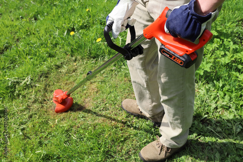 Foto Man holds an electric trimmer in his hands and mow grass in meadow, on sunny day