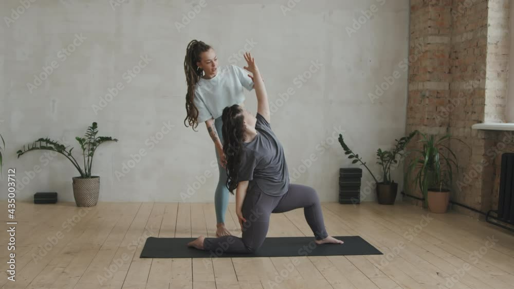 Full shot of young woman with down syndrome learning basic asanas with female yoga coach helping her having individual class in bright modern yoga studio Full shot of young woman with down syndrome learning basic asanas with female yoga coach helping her having individual class in bright modern yoga studio