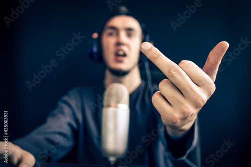 Streamer show gestures. Man lose game and shows the middle finger. Guy with headphones in front of a vintage microphone. Voice recording for games.