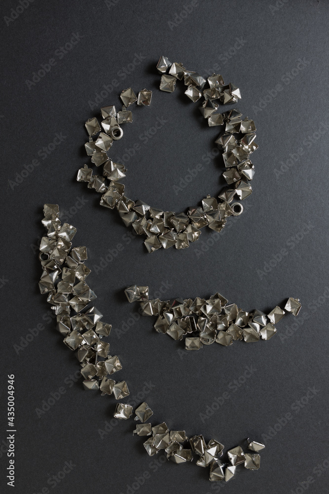 old, worn, recycled square pyramidal leather-craft metallic studs or spikes arranged on a dark grey mat board with low or raking light - photographed from above in a flay lay composition old, worn, recycled square pyramidal leather-craft metallic studs or spikes arranged on a dark grey mat board with low or raking light - photographed from above in a flay lay composition