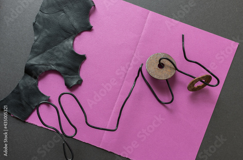 composition with magenta pink construction paper, black plastic coated wire, rusty metal washer, and leather piece 