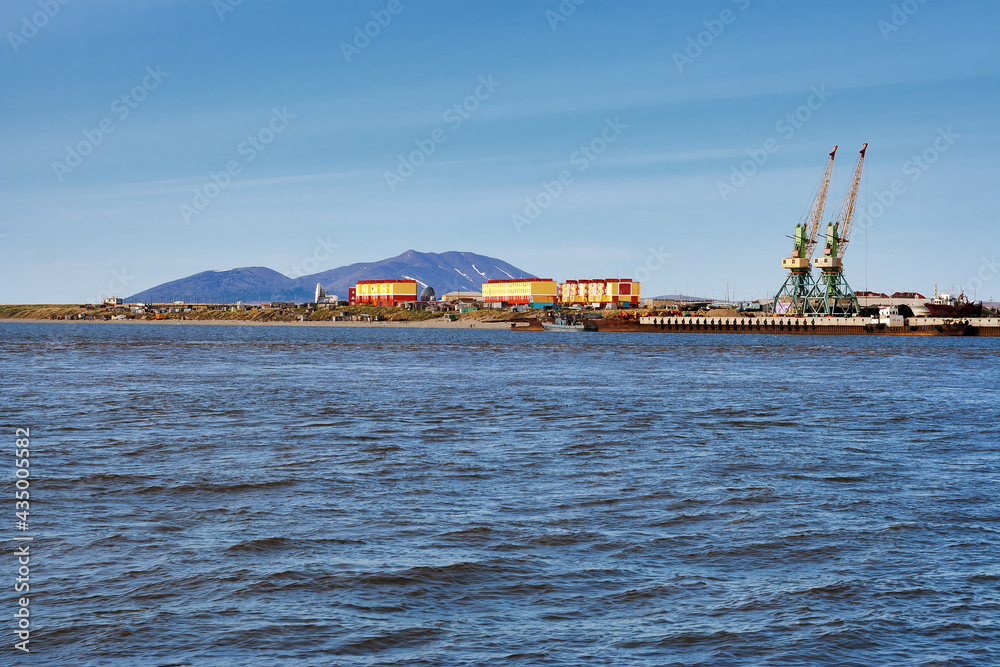 Summer arctic landscape. View from the sea to the coastal settlement and the cargo port. Colorful buildings on a background of mountains. Tavayvaam village, Chukotka, Siberia, Far East of Russia.