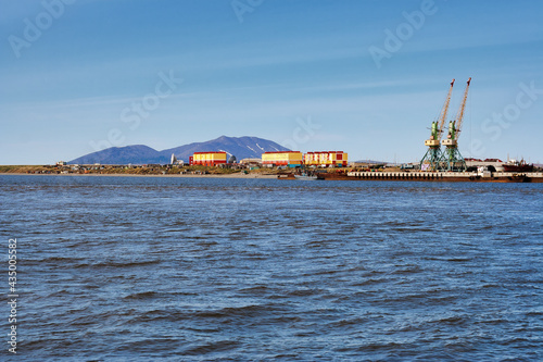 Summer arctic landscape. View from the sea to the coastal settlement and the cargo port. Colorful buildings on a background of mountains. Tavayvaam village, Chukotka, Siberia, Far East of Russia.