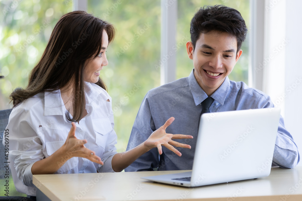 Beautiful black long hair Asian businesswoman and gook looking cute Asian businessman sitting together and watching the screen of laptop notebook computer in office with smile face Beautiful black long hair Asian businesswoman and gook looking cute Asian businessman sitting together and watching the screen of laptop notebook computer in office with smile face
