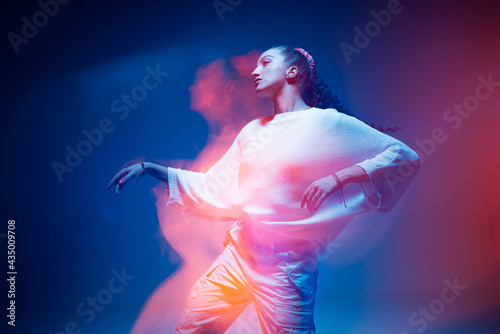 Fototapeta Naklejka Na Ścianę i Meble -  Mixed race young modern girl dancing in colourful neon light. Long exposure. Stylish female moving to rap rhythm